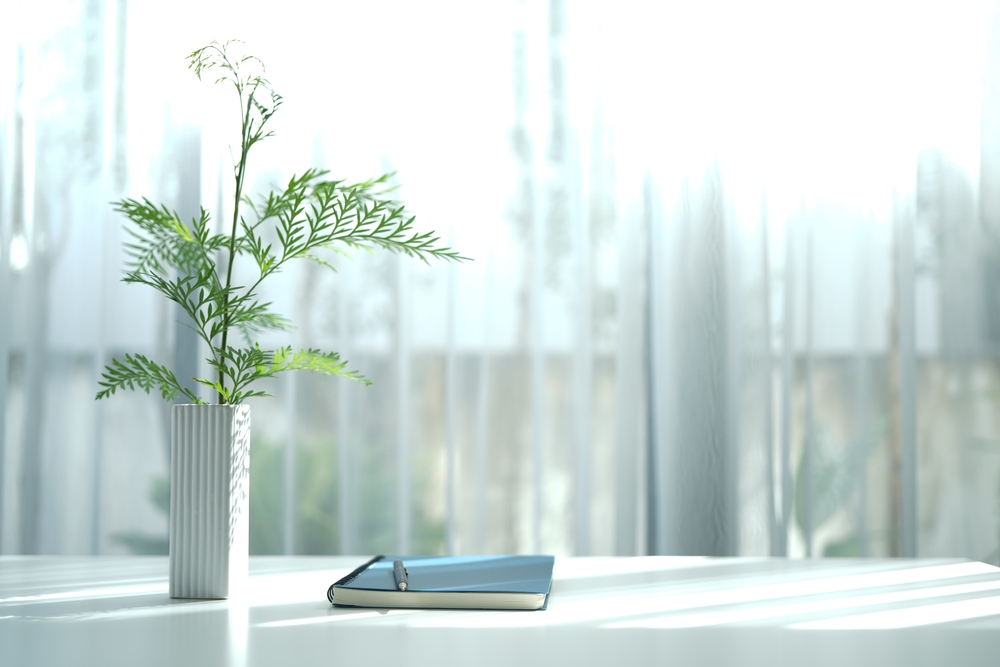 A plant vase and a notebook on a clean white table.
