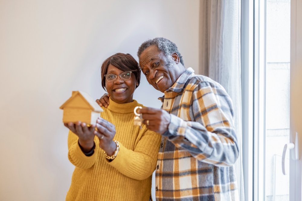 A senior couple holding a model house and a set of keys.