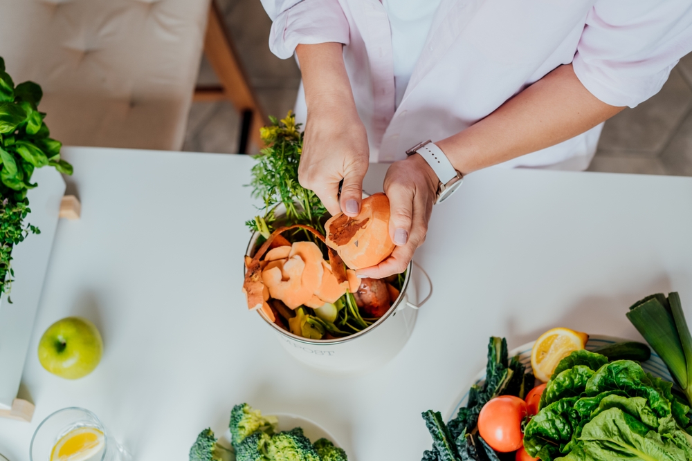 An image of a person peeling a vegetable and putting the peel in a compost container.