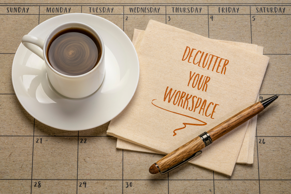 An image of a cup of coffee and a calendar, with a pen and paper that reads: "Declutter Your Workplace"