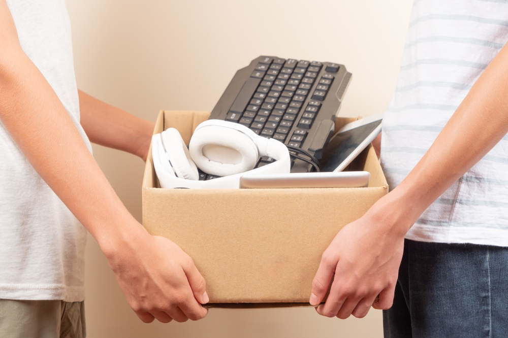 A person handing over a box of donated electronics to another person.