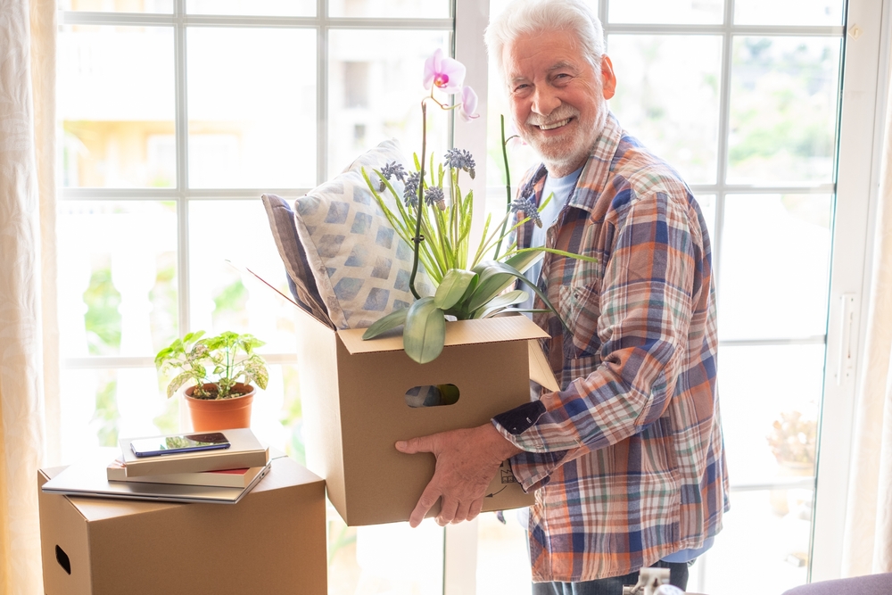 A senior smiling and holding a box of potted plants.