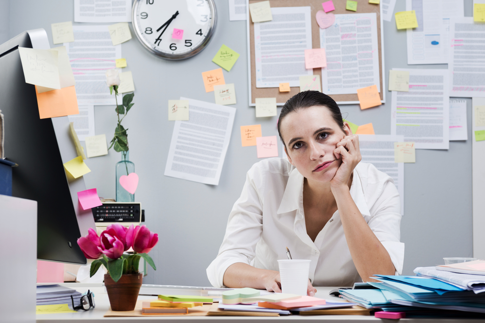 An image of a tired businesswoman at a messy cubicle.
