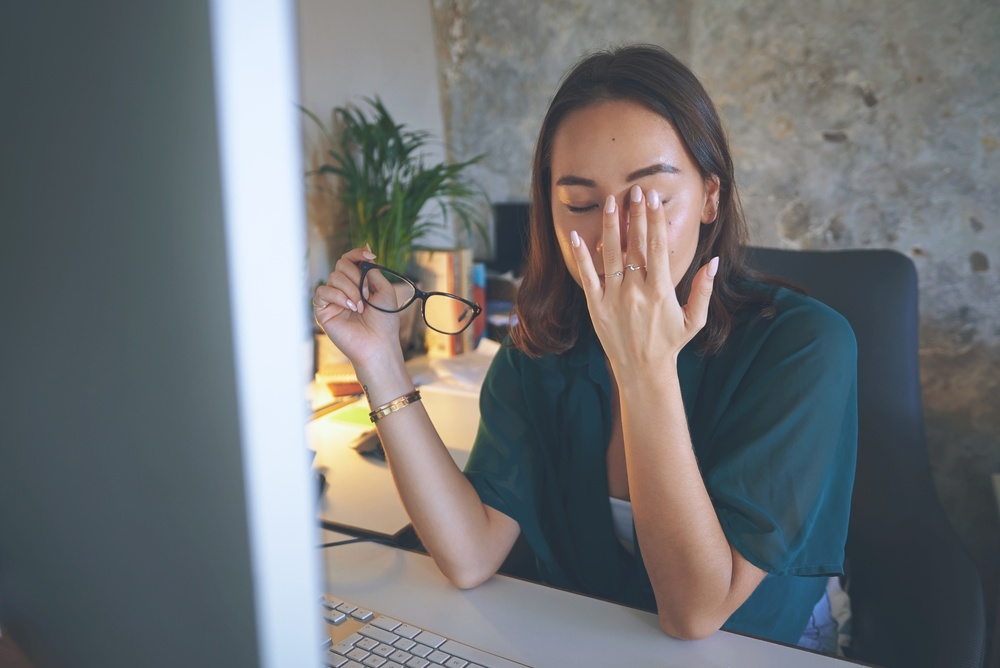 A person with a headache from digital clutter sitting at a computer desk.