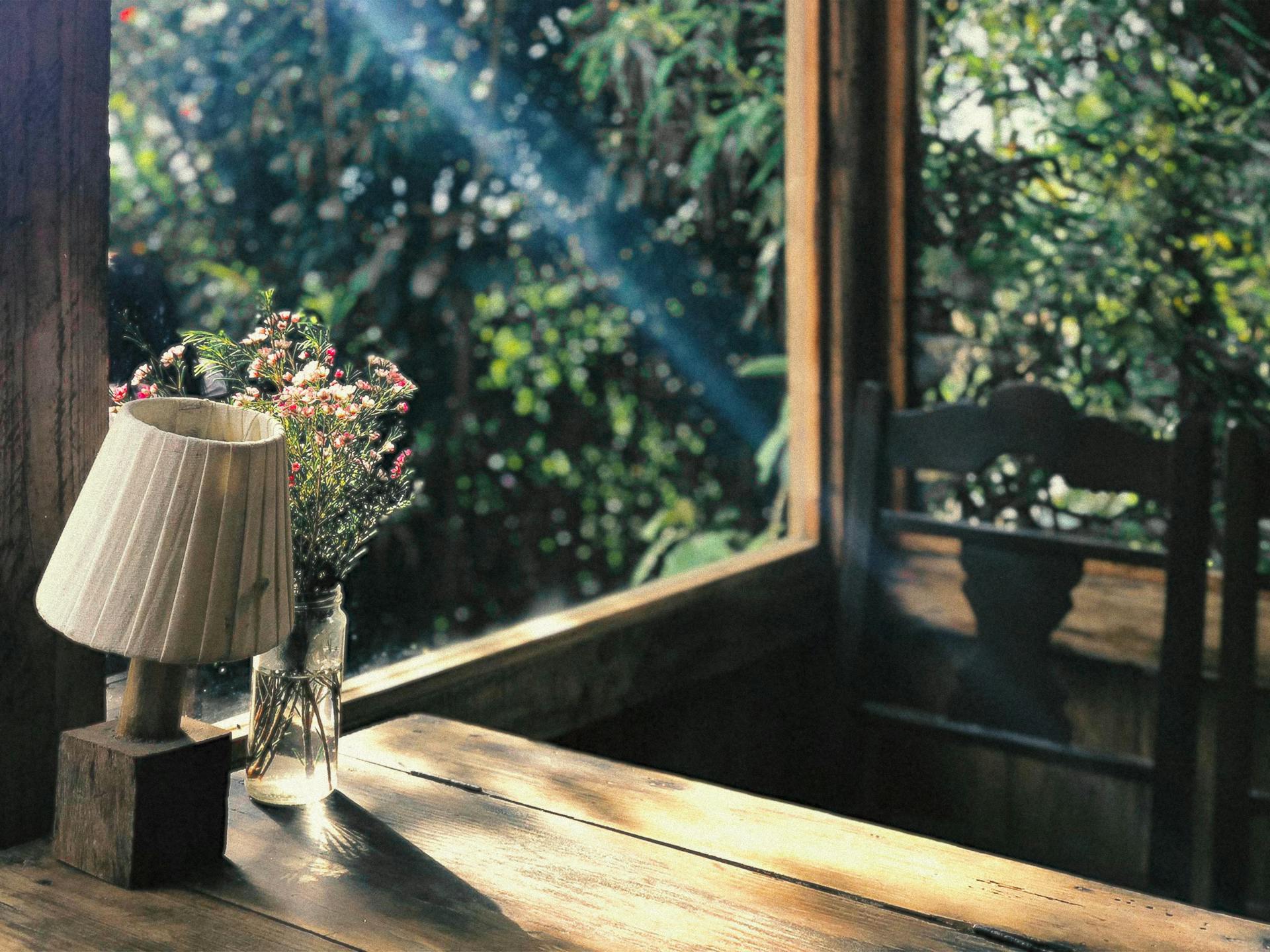 An image of sunlight flowing through a window of a room with a table, chair, and lamp.