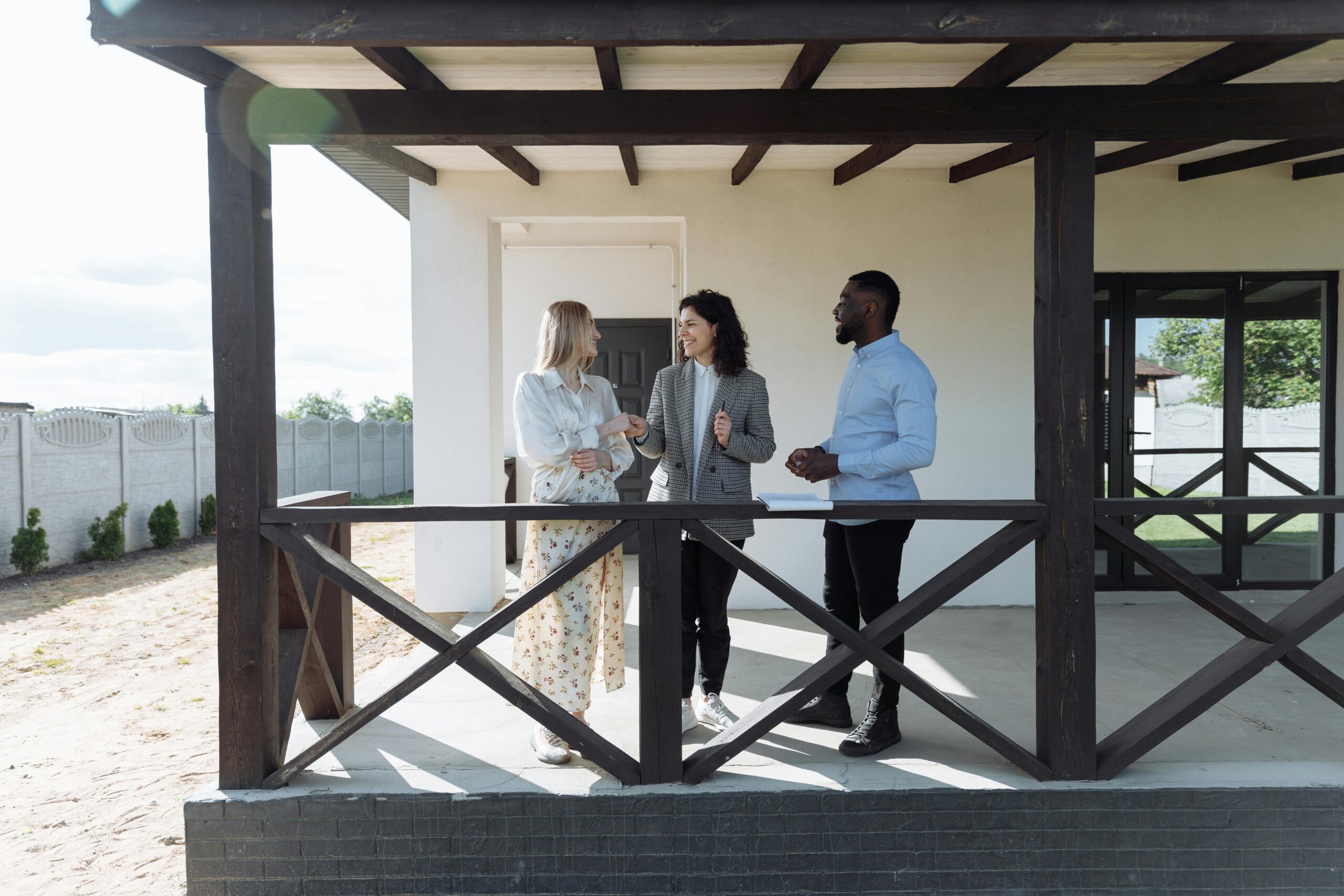 An image of a realtor talking to a couple on the porch of a house.