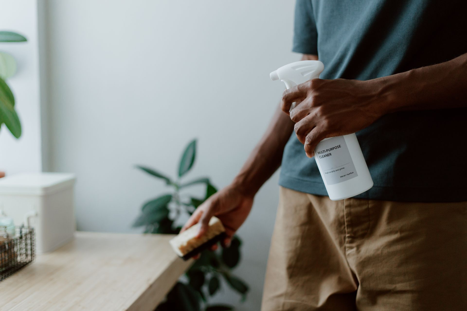 An image of a man holding a bottle of cleaning solution and a sponge.