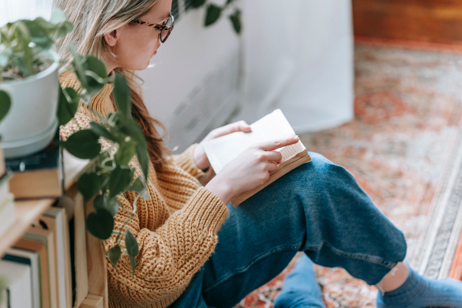An image of a woman reading a book next to a bookshelf.