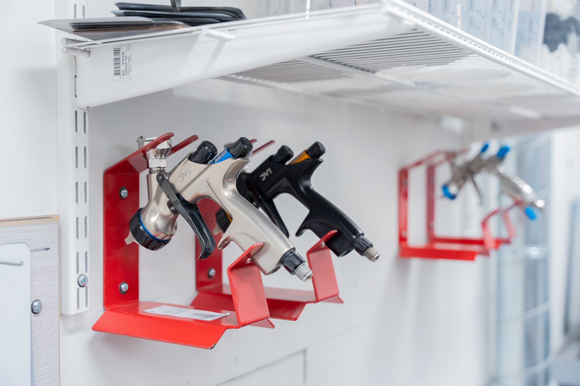An image of spray guns for automobile painting arranged neatly on wall racks.