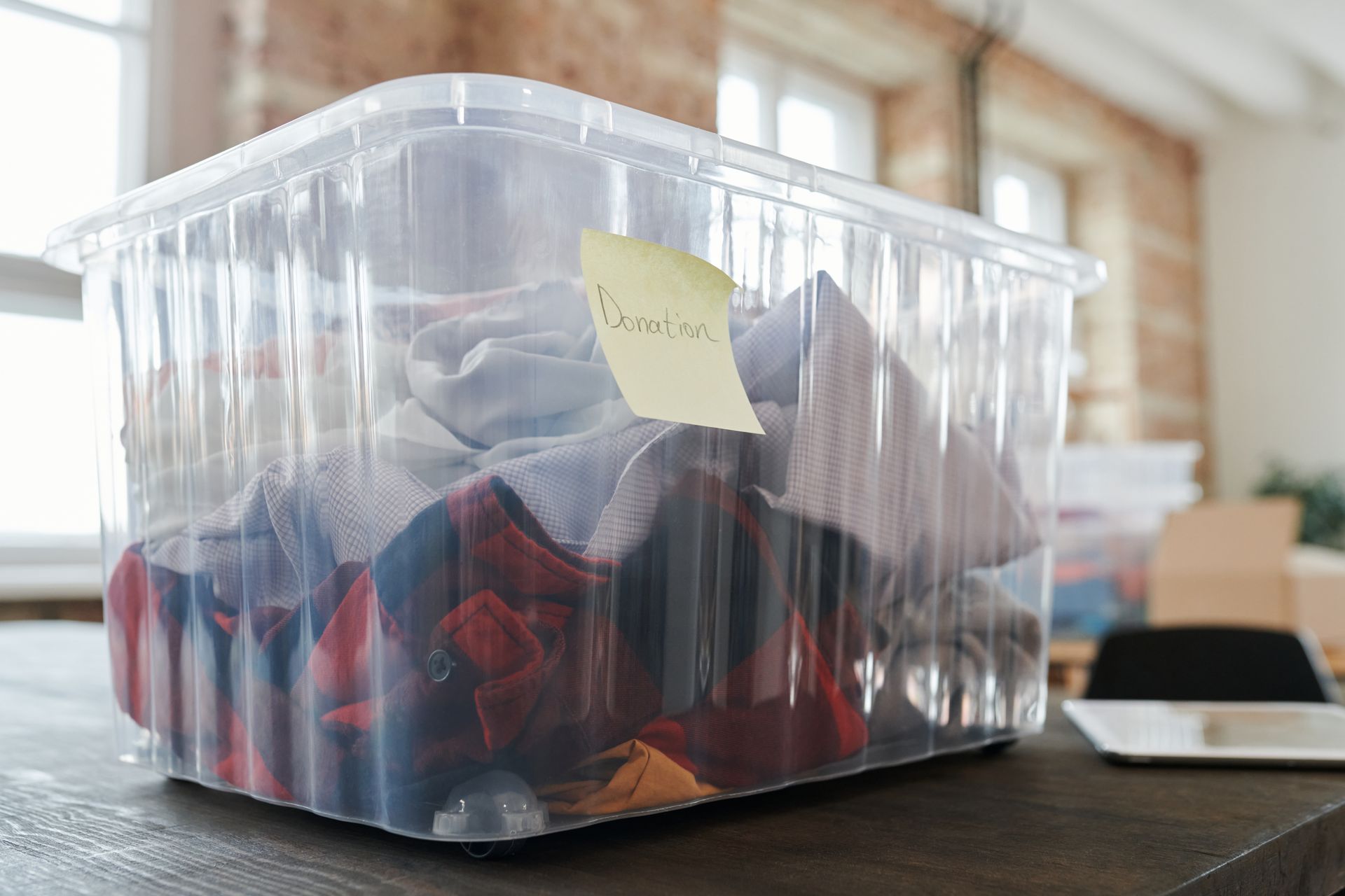 An image of a clear bin labeled "Donations" with clothes inside.